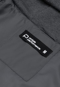 Tela de chaqueta gris con una textura suave, que presenta una etiqueta negra que dice "ontbe performance" y la talla "M" en letras blancas.