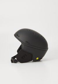 Svart ski-hjelm med matt finish, justerbart hakestropp, ventilasjonsåpninger, og et klart gult sertifiseringsklistremerke på siden.