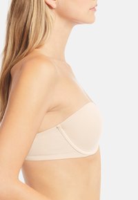 Beige strapless bra dengan tekstur halus dan bentuk melengkung, dilengkapi dengan cawan tanpa sambungan dan pengikat di sisi.