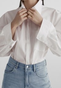 Biała bawełniana koszula zapinana na guziki z kieszenią, oversize'owymi rękawami i gładką fakturą, zestawiona z jasnoniebieskimi, wysokim stanem dżinsami.