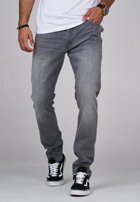 Jeans in denim grigio con una vestibilità slim, caratterizzati da un classico design a cinque tasche. Indossati con sneakers in bianco e nero, evidenziando uno stile casual.