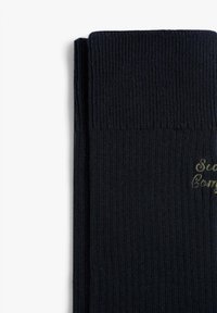 Calcetines de color navy con canalé, con un puño doblado y detalle del logo bordado en dorado en el lateral. Textura suave con un ajuste ceñido.