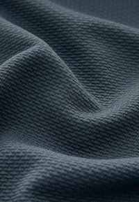 Tissu gris foncé avec une petite texture gaufrée en relief, présenté en plis doux et avec un éclairage doux.