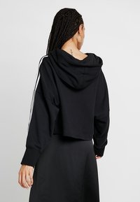 Sudadera corta con capucha de color negro, hecha de un material suave, con mangas largas y franjas blancas a los lados. Sin patrones ni acentos visibles.