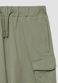 Hellgrüne Cargo-Hosen mit elastischem Bund. Verfügt über einen Kordelzug und eine Seitentasche mit Klappe. Weicher, strukturierter Stoff.