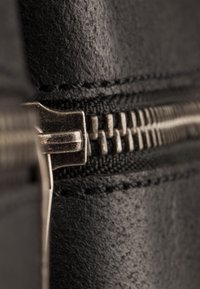 Zwart leren materiaal met een zilveren metalen rits, met verhoogde stiksels langs de rand en zichtbare rits tanden. Close-up weergave.