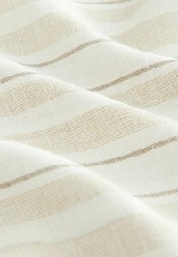 Tissu léger avec un motif texturé en rayures beige et crème, affichant une finition douce et tissée avec des variations de design subtiles.