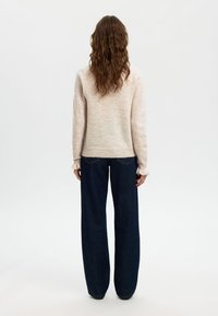 Gaiši rozā adīts džemperis ar garām piedurknēm un kroku aprocēm, kombinēts ar tumši zilām plaša piegriezuma džinsa biksēm. Mīksta tekstūra un brīvs piegriezums.