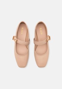 Bailarinas beige con punta cuadrada, tira elástica y detalle de hebilla dorada. Material suave similar al cuero con un forro interior suave.