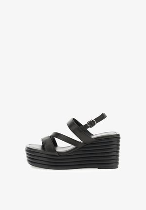 Sandalias de cuña negras con diseño de múltiples correas cruzadas, hebilla ajustable en el tobillo y plataforma texturizada. Material de cuero suave.