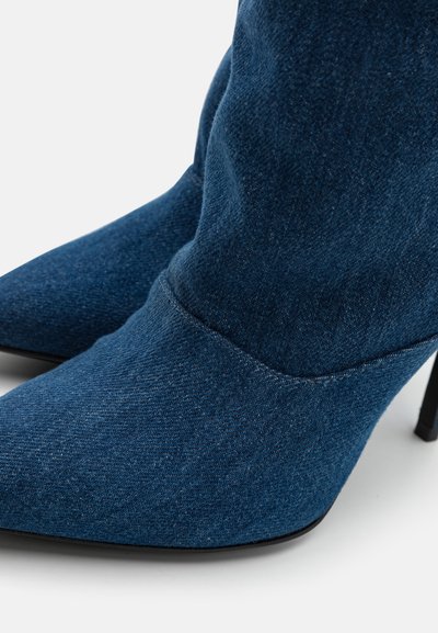 Stivaletti in denim con punta affusolata, alti tacchi a stiletto e dettagli cuciti in tessuto blu scuro, caratterizzati da una texture liscia.