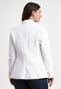 Λευκό κομψό σακάκι με δομημένο γιακά και τρία κουμπιά στα μανίκια, κατασκευασμένο από απαλό ύφασμα με κομψή εφαρμογή.