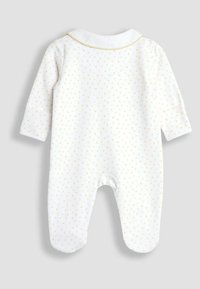 Un body en coton blanc pour bébé avec des pois dorés, à manches longues, avec des poignets aux chevilles et un col blanc, orné d'une chaîne décorative dorée autour du cou.