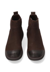 Brązowe skórzane botki z gładkim, matowym wykończeniem, zaokrąglonym noskiem oraz kontrastującą połyskliwą nasadką na palcach. Posiadają pętelki ułatwiające zakładanie.