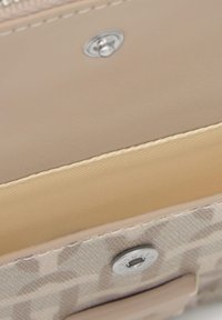 Beige leather interior with smooth texture, featuring a silver button closure. Patterned fabric visible at the bottom, with contrasting stitching.