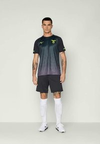 Pánsky čierny a tmavosivý futbalový dres so žltými akcentmi a logom, v kombinácii s čiernymi šortkami, bielymi ponožkami a kopačkami. Hladká textúra látky.