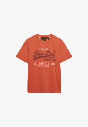 Maglietta arancione a maniche corte con logo vintage SuperDry, testo giapponese e "TEE. SHIRT. STORE. TOKYO, JAPAN." stampati sul davanti.
