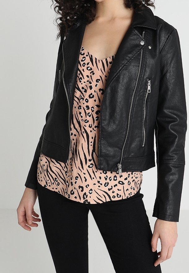 Veste de motard en similicuir noir avec des fermetures éclair et des boutons-pression argentés, portée sur un haut léopard rose, associée à un pantalon noir.