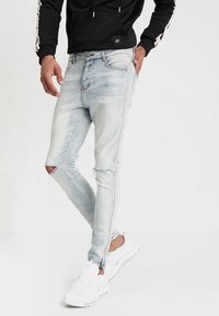 Hellblaue Skinny-Jeans mit Distressed-Effekten an den Knien, seitlichen Streifen und einem ausgeblichenen Finish. Kombiniert mit weißen Sneakers.