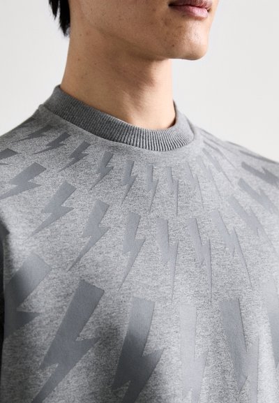 Grå sweatshirt med ribbad rundhals och präglat blixtmönster över bröstet, tillverkad av mjukt tyg.