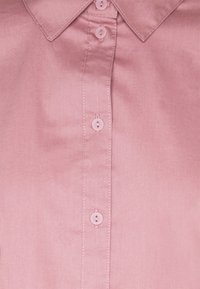 Light pink button-up shirt with a collar, featuring six buttons and a smooth, glossy texture. Includes subtle stitching details.
