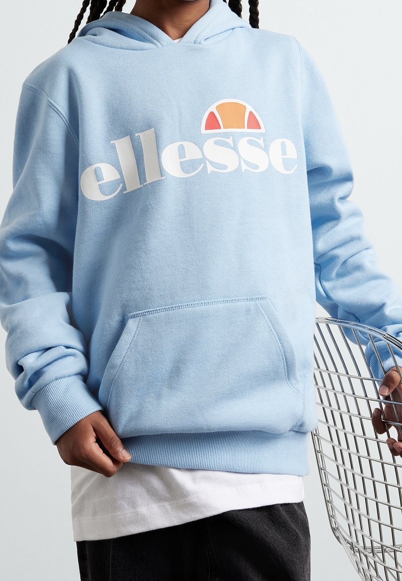 Sweat à capuche bleu clair en matériau doux avec un grand logo blanc et un graphisme coloré au-dessus. Comprend une poche avant et des poignets côtelés.