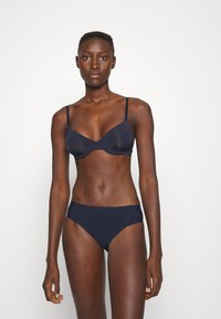Navy blue bra with thin adjustable straps and soft cups, paired with matching low-rise bikini briefs, all in a smooth, stretchy fabric.