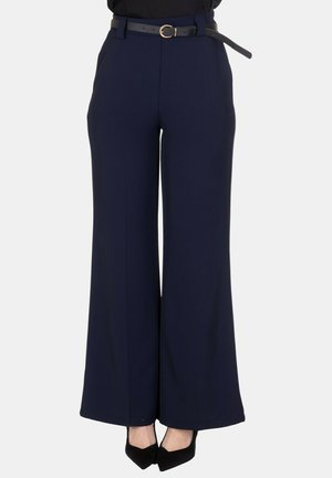 Pantaloni ampi blu navy a vita alta, abbinati a tacchi neri con punta appuntita e una cintura sottile nera con fibbia dorata.