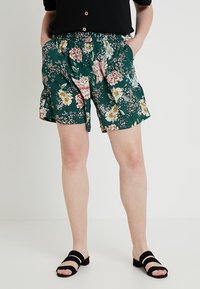 Blommiga shorts i grönt med elastisk midja och sidfickor. Tillverkade av lätt tyg med rosa, gula och vita blommor.