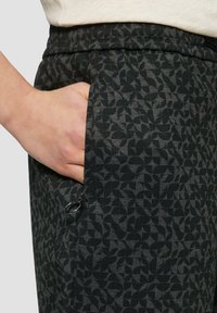 Zwarte gestreepte broek met een geometrisch patroon, elastische tailleband en een zijzak met ritssluiting.