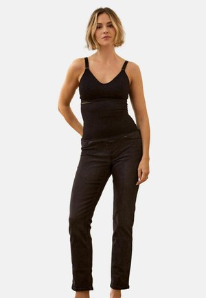 Canotta aderente nera con spalline larghe e scollo a V, abbinata a jeans scuri a taglio slim. Design semplice senza motivi o dettagli visibili.