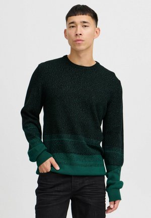 Dark green knit sweater with textured patterns, crew neckline, and ribbed cuffs. Fabric features varying shades from dark to lighter green.
