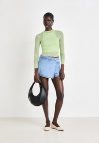 Light green, textured long-sleeve top; denim wrap mini skirt; black handbag; beige flat shoes; neutral backdrop.