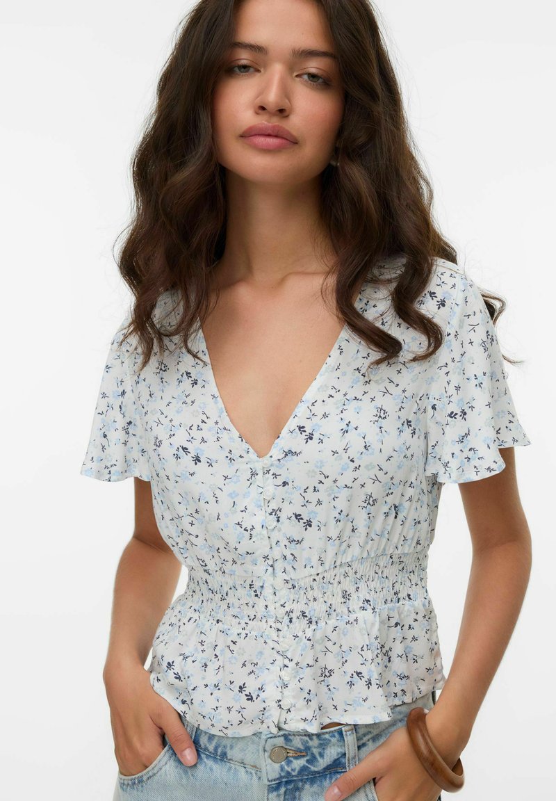 Blusa floreale in azzurro chiaro, con maniche corte a volant, scollatura a V profonda e vita arricciata. Realizzata in tessuto morbido e leggero.