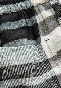 Tela de cuadros en blanco y negro con rayas horizontales y verticales, con un acabado texturizado y una cintura elástica. Incluye un pequeño bolsillo.