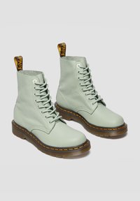 Botas de cuero verde menta hasta el tobillo, con puntera redonda, cordones en la parte delantera, costuras amarillas en contraste y una pestaña en el talón. Suela de goma plana.