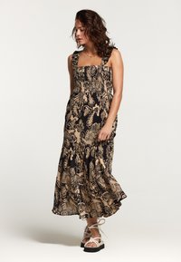 Rochie Maxi în negru și bej, cu modele florale, cu un bust elastic, bretele late și o fustă evazată. Purtați cu sandale albe cu curele.