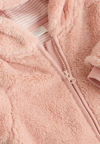 Veste zippée en polaire rose et moelleux avec une doublure intérieure rayée et des poignets doux. Elle possède une fermeture éclair à l'avant et une étiquette avec "NEXT Baby".