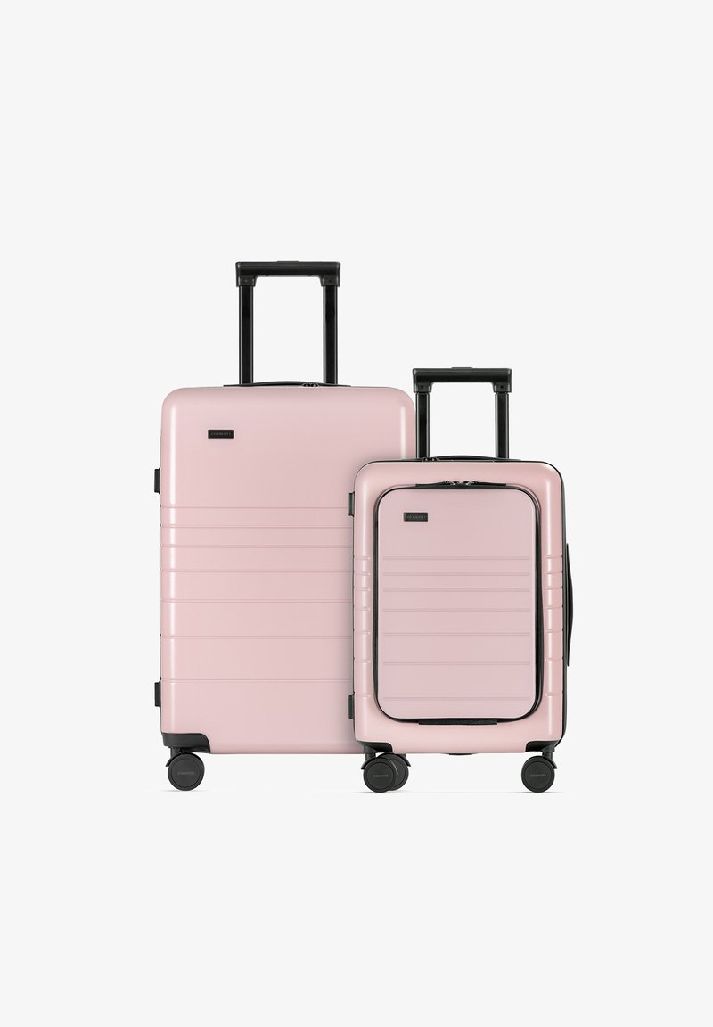 Dwie różowe walizki twarde, jedna duża i jedna mała, z teksturowanymi panelami bocznymi, czarnymi akcentami i czterema kołami dla łatwej mobilności.