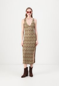 Abito in maglia con motivo a zig zag in tonalità terrose, con scollatura a V profonda, spacco laterale, abbinato a stivaletti alla caviglia marroni.