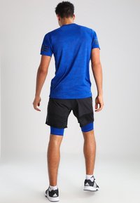 Blå atletisk t-shirt med ett subtilt mönster, parat med svarta shorts och blå kompressionsbyxor, med svarta atletiska skor.