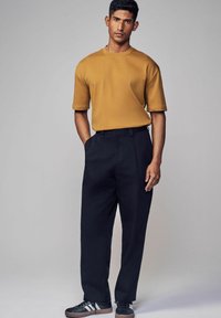 Kortærmet sennepsfarvet t-shirt parret med høj talje sorte bukser og mørke sneakers med hvide detaljer. Enkel, moderne design.