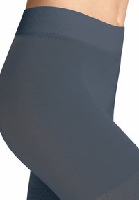 Leggings attillati di colore grigio scuro su una persona, che mostrano texture e dettagli dell'elastico in vita e sulla coscia superiore.