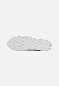 White sneaker outsole featuring a textured rubber surface with a circular logo and various grooves for traction. Minimalist design, flat profile.