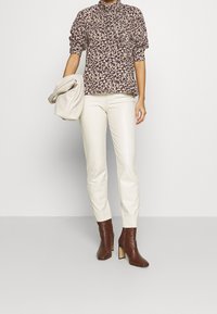Knopfbluse mit einem mehrfarbigen Blumenmuster, kurzen Puffärmeln; kombiniert mit crèmefarbenen, schmal geschnittenen Hosen und braunen, heeled Stiefeletten.