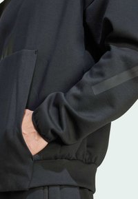 Black sweatshirt featuring a front pocket, elastic cuffs, and a matte finish on the left sleeve. Smooth fabric with minimal design accents.