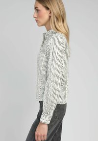 Chemise à rayures noire et blanche avec un col haut, des manches longues et de petites découpes le long de la patte de boutonnage.