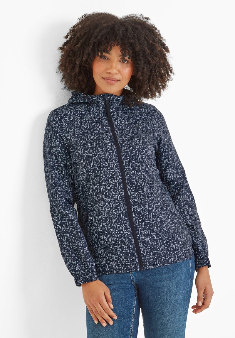 Navy hooded jacket with a white leaf pattern, zip closure, and elastic cuffs. Worn with blue jeans, featuring a relaxed fit and lightweight material.