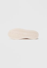 Suela de una zapatilla, con una superficie de goma texturizada en rosa pálido, diseñada con un patrón de espiga y un acento circular en el centro.