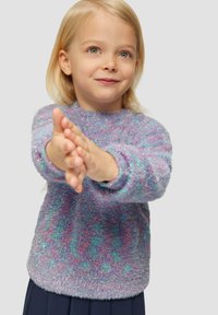 Un pull en peluche violet et teal avec un col rond, des manches longues et une texture pailletée, porté avec une jupe marine. Un enfant tend les mains en avant.